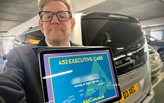 Chauffeur holding digital airport meet and greet sign beside Mercedes V-Class
