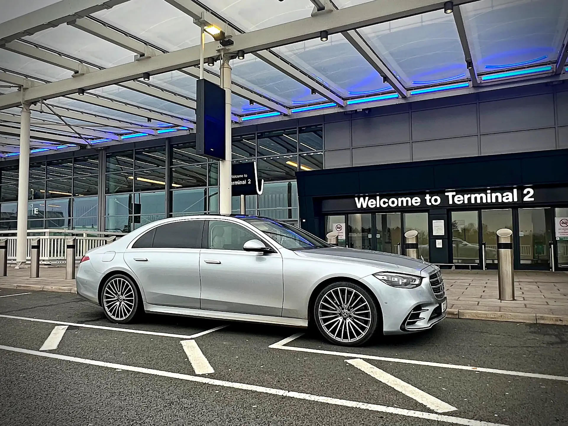 Mercedes S Class chauffeur vehicle outside airport terminal for executive transfer